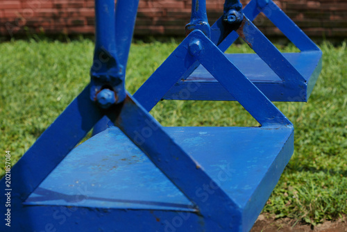 Close-up seat on the iron swing game outdoor playground with geometric triangular structure, on a grassy field.