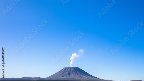 Small volcanic vent emitting a plume of smoke against a clear blue sky, landscape view.