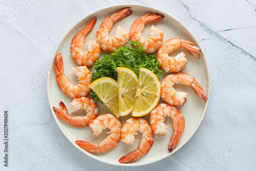 A top-down shot of several peeled and deveined cooked shrimps arranged in a circular pattern on a white plate.