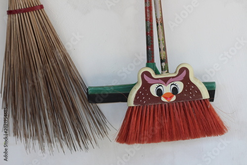 Traditional wooden stick broom and a cute owl-shaped plastic broom leaning against a white wall