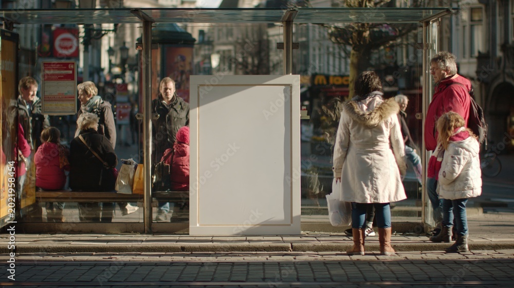 Obraz premium Diverse group of people waiting at a sunny urban bus stop with a blank advertisement panel