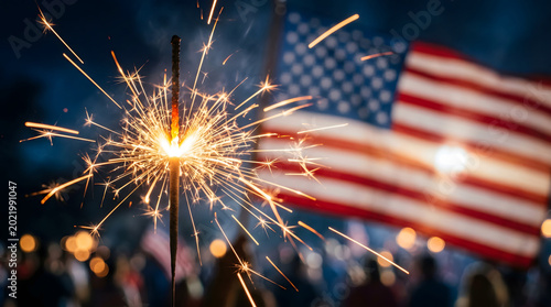 Sparkling handheld sparkler with American flag background, glowing Fourth of July celebration, patriotic holiday night with golden bokeh lights