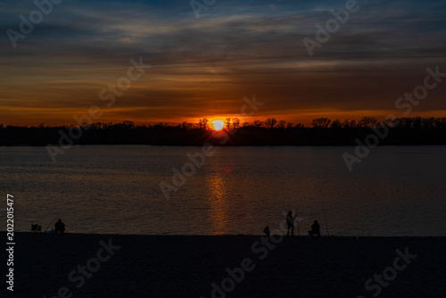 Fishermen at the bank of the river at sunset. Silhouette photo
