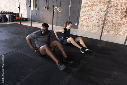 Quadro em tela Diverse workout partners doing floor tricep dips on rubber mats near metal rig w