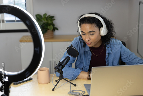 Nonbinary person wearing denim jacket and white headset recording podcast with mic laptop in studio