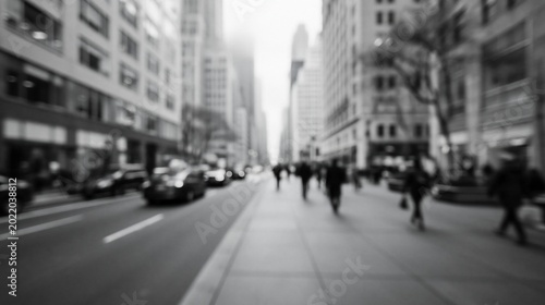 Black and white photo of a bustling city street with blurred pedestrians and cars, capturing urban energy