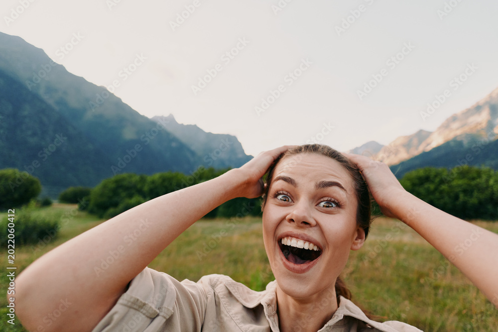 Fototapeta premium Cheerful woman outdoors, wide smile, hands on head, sunlight moment in a mountains valley, relaxed posture, vibrant natural colors, fresh air, happiness, lifestyle, nature, bright