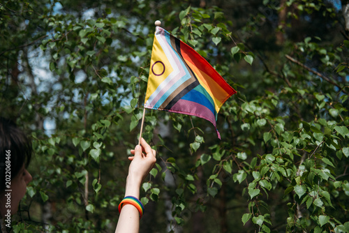 Hand holds inclusive pride flag against foliage. lgbtq diversity and inclusion, corporate pride support, lgbtq friendly business.
