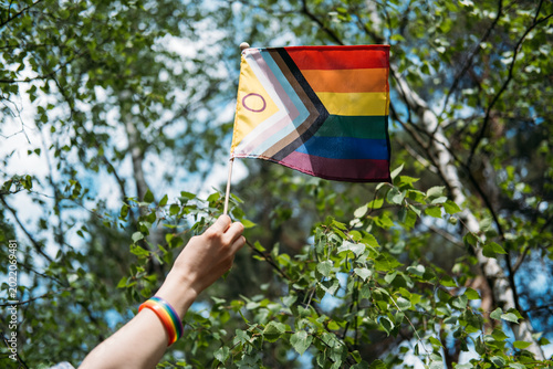 Hand holds inclusive pride flag toward sky. LGBTQ Identity, gender expression, authentic self, pride symbol.