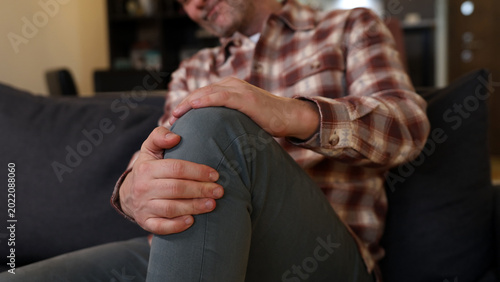 Foto Man at home holding painful injured knee.