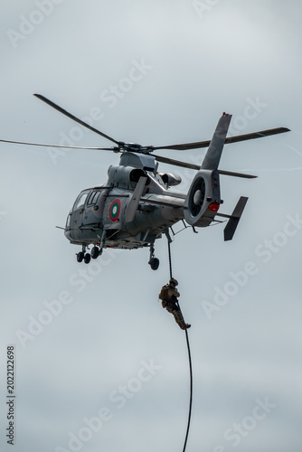 Elite special forces operator fast-roping from a hovering military helicopter during a tactical insertion or rescue mission
