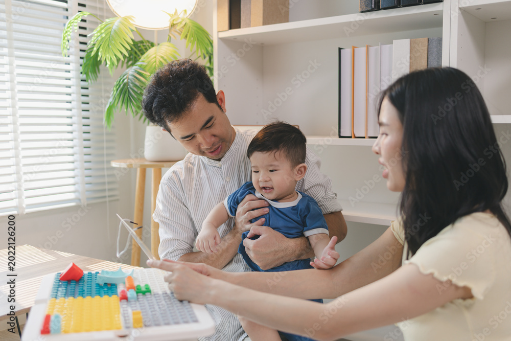 Obraz premium Happy young family playing with baby at home, parents engaging child with colorful toys and learning activities, showing love, care, early childhood development, and warm bonding moment together.
