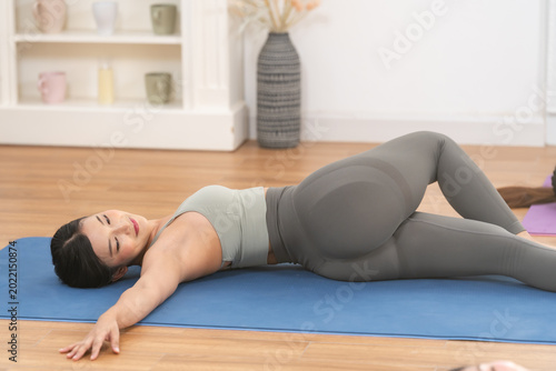 Foto Asian adult woman performs supine spinal twist on blue mat, arms open, knees ben