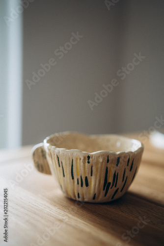 Beige handmade ceramic mug with carved texture lines and hand-painted abstract blue and yellow strokes.