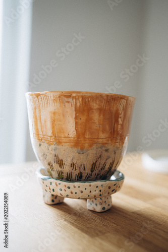 Minimalist two-tone handmade ceramic flower pot, half orange and half beige, on a small legged stand.