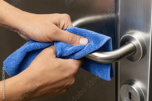 Hands cleaning a metal door handle with a blue microfiber cloth in a sharp focus macro shot for hygiene and janitorial service marketing