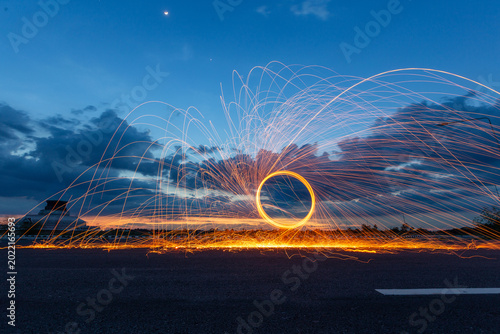Canvas-taulu Spinning burning steel wool creates glowing spark trails in a circle at twilight with a temple stupa in the background