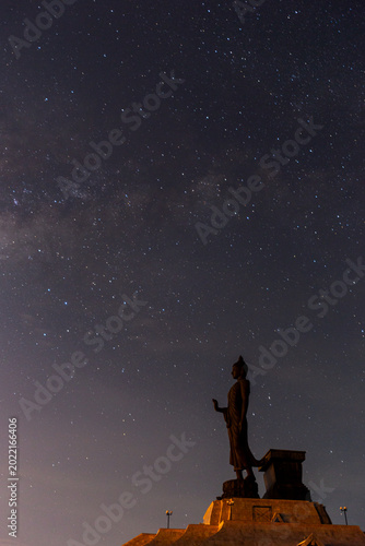 Obraz na płótnie Wide view of a tall standing Buddha monument dramatically silhouetted under a spectacular starry night sky
