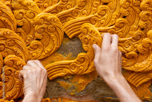 Tableau sur toile Close up of artisan hands carving intricate Thai patterns on a large yellow wax sculpture for a traditional festival