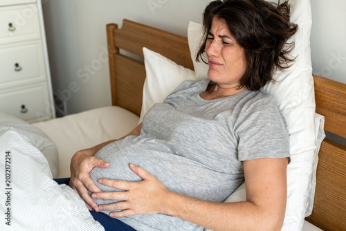 Fotografie Pregnant woman in discomfort lying in bed, holding her belly.