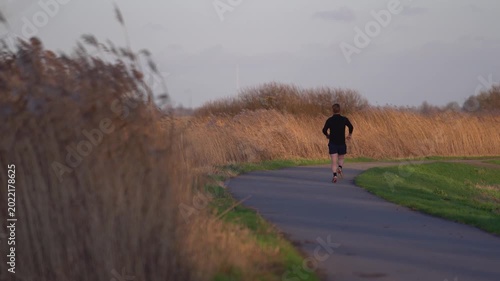 Man Jogging on Rural Path at Sunset Near Tall Reeds in February