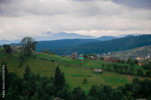 Picturesque mountain landscape. Ukrainian Carpathians. A cozy village lies in the valley below, surrounded by rolling green hills and misty mountain peaks. Bright traditional houses and untouched