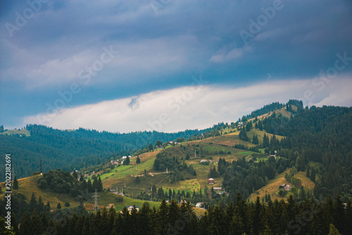 Picturesque mountain landscape. Ukrainian Carpathians. A cozy village lies in the valley below, surrounded by rolling green hills and misty mountain peaks. Bright traditional houses and untouched