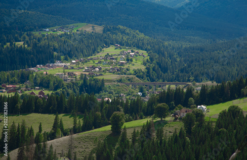 Picturesque mountain landscape. Ukrainian Carpathians. A cozy village lies in the valley below, surrounded by rolling green hills and misty mountain peaks. Bright traditional houses and untouched