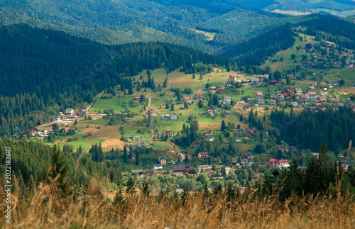 Picturesque mountain landscape. Ukrainian Carpathians. A cozy village lies in the valley below, surrounded by rolling green hills and misty mountain peaks. Bright traditional houses and untouched