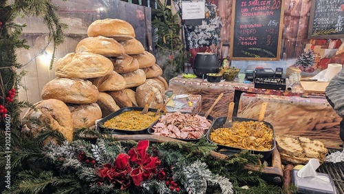 Festive Christmas market food stall with stacked rustic bread, hot traditional dishes, menu boards, evergreen decorations, and warm winter market atmosphere.