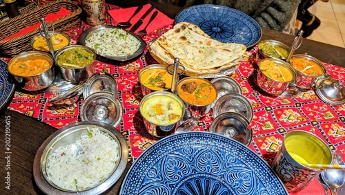 Traditional Indian food spread with curry dishes, basmati rice, naan bread, sauces, and colorful table setting in a restaurant.