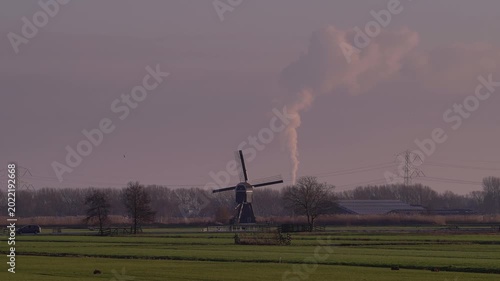 Traditional Dutch Windmill Contrasted with Industrial Pollution in the Distance