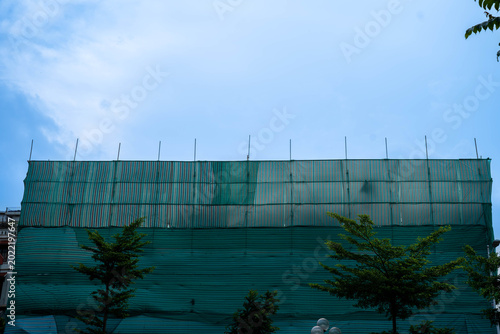Fotografija Construction site covered with green mesh and blue sky, showcasing urban development