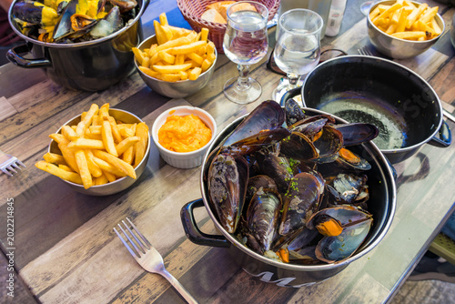 Moules Frites French Mussels in Black Pot With French Fries and Sauce on Wooden Table