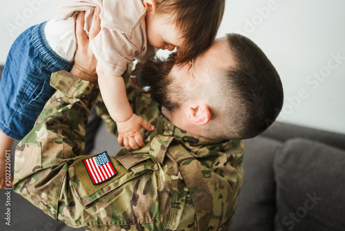 Foto Male american soldier in military uniform hugs his little son at home - Emotiona