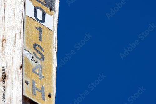 Fotografía Quebec, Canada, 26 April 2026 : A weathered wooden pole features a yellow and white identification marker with black alphanumeric characters against a blue sky