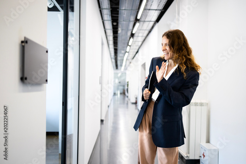 Bilde på lerret Businesswoman entering office hallway, waving hand, greeting colleagues, fosteri