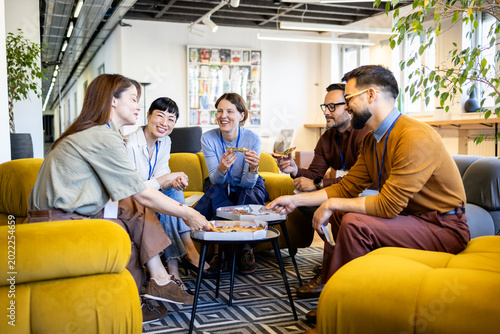 Diverse business team sharing pizza during casual lunch break, enjoying friendly conversation in modern office lounge area