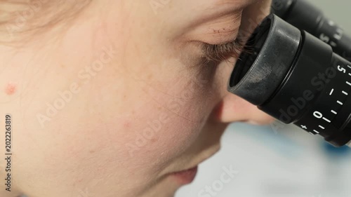 Gynecologist examines Pap test sample through microscope in close view. Specialist studies specimen carefully checking optical focus during review