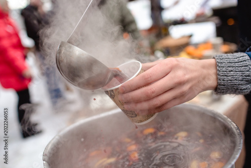 Obraz na płótnie Person pouring steaming hot mulled wine from a large metal pot into a paper cup using a ladle at an outdoor winter market