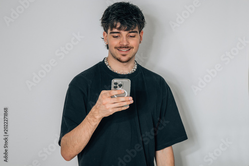 Young man in black t-shirt smiling while looking at his phone. Clean studio background, casual style, natural light, perfect for lifestyle and tech concepts