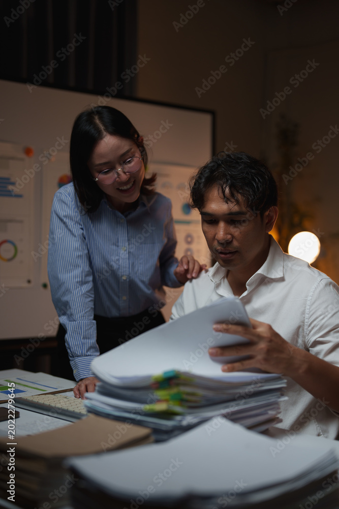 Naklejka premium Two business people collaborating on a project, analyzing data and reviewing documents late at night, working overtime in an office toward a deadline