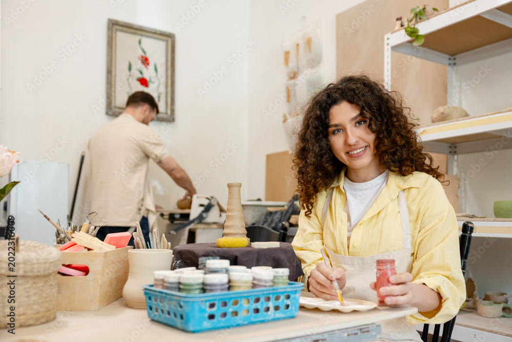Fototapeta premium Woman ceramicist painting handmade pottery in workshop