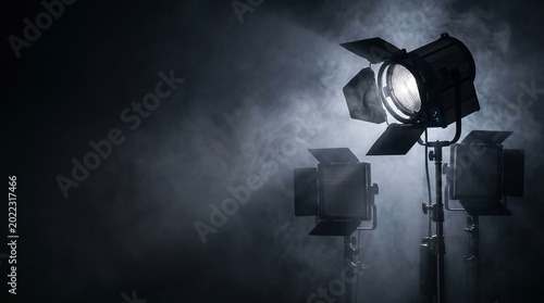 Powerful studio lights pierce through dense smoke on a dark stage, creating a dramatic and atmospheric scene perfect for filmmaking, photography, or live event production