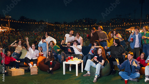 Obraz na płótnie Excited crowd of friends celebrating outdoor sports viewing party at night