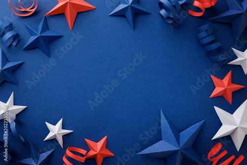 Festive arrangement of red, white and blue paper stars and curled ribbons on dark blue background. Patriotic border with empty space for text, suitable for Independence, Fourth of July, Memorial