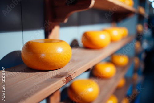 Photos orizontal close-up of a whole Dutch Gouda cheese wheel with a classic orange wax coating, maturing on a rustic wooden shelf