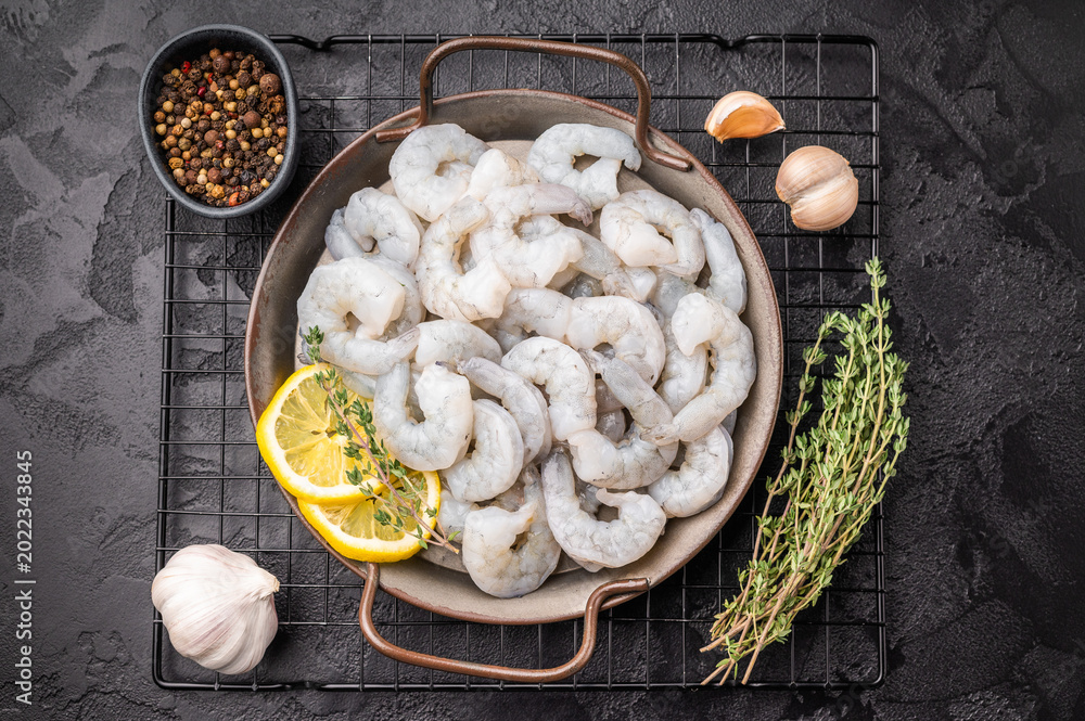 Fototapeta premium Uncooked prawns shrimps ready for gourmet cooking. Dark, moody shot with citrus and herbs. Negative space for text.