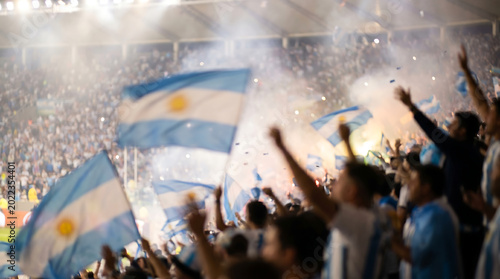 Argentina flags waving with fans in an intentionally blurred football stadium celebrating a soccer match victory for background design