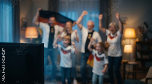 German football fans family cheering in cozy living room with TV foreground intentationally blurred background for sports celebration